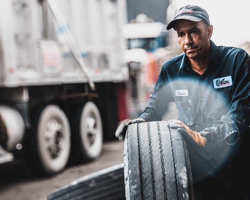 Alex Truck Tire technician carrying a truck tire in the shop